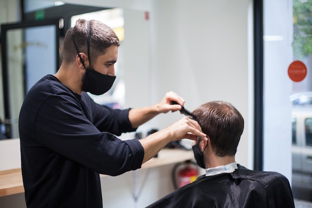 Un parrucchiere professionista che indossa una maschera protettiva che taglia i capelli a un cliente durante il coronavirus