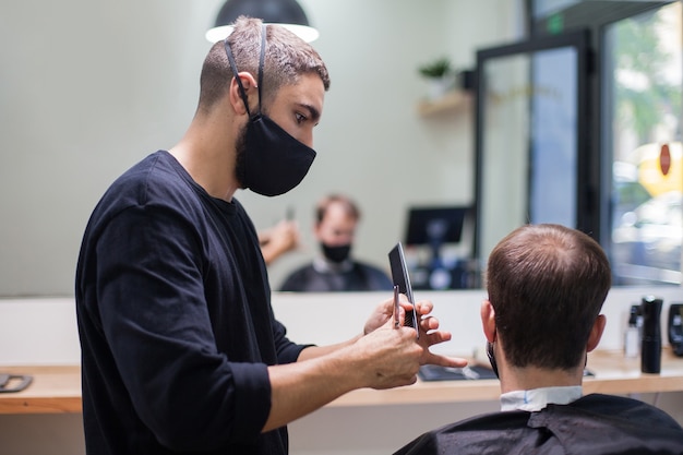 Un parrucchiere professionista che indossa una maschera protettiva che taglia i capelli a un cliente durante il coronavirus