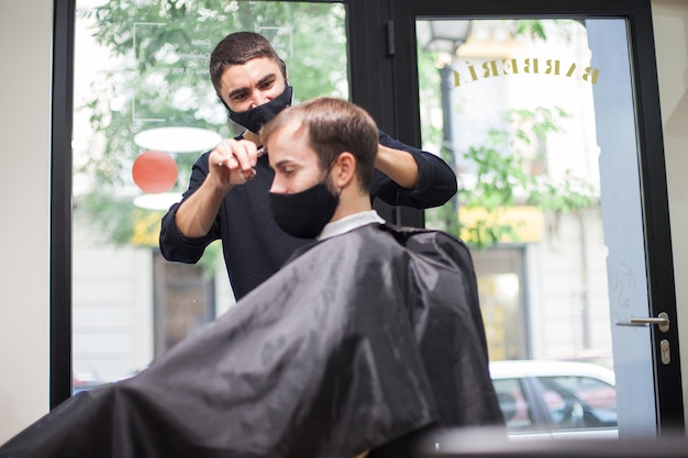 Foto un parrucchiere professionista che indossa una maschera protettiva che taglia i capelli a un cliente durante il coronavirus