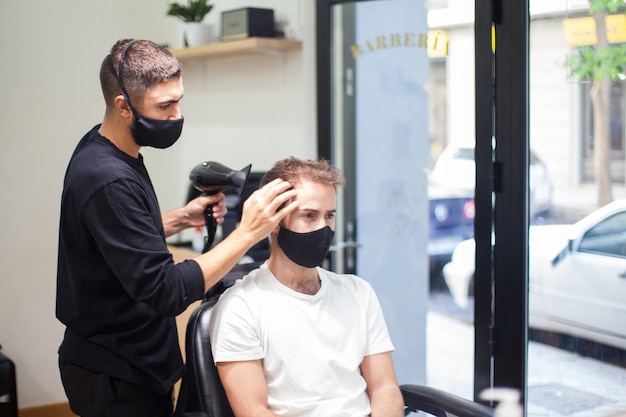 Un parrucchiere professionista che indossa una maschera protettiva che taglia i capelli a un cliente durante il coronavirus