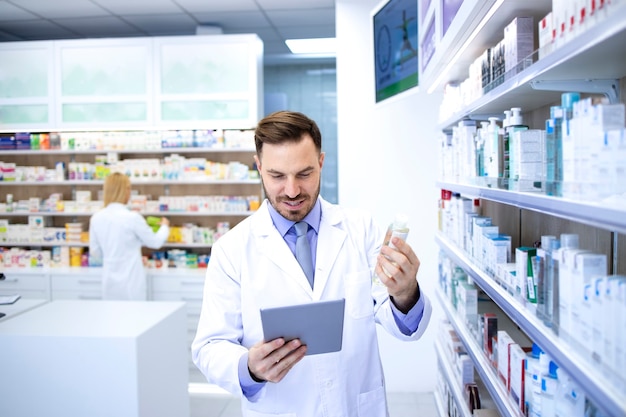 Professional handsome male pharmacist working in pharmacy store or drugstore and checking medicines on his tablet computer.