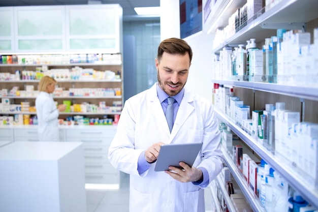 Professional handsome male pharmacist working in pharmacy store or drugstore and checking medicines on his tablet computer.