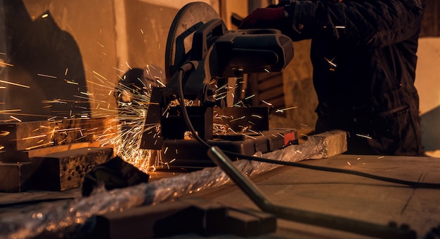 Professional hardworking man cutting or grinding metal surface on grinder machine and sparks at the factory of metalworking machining industry