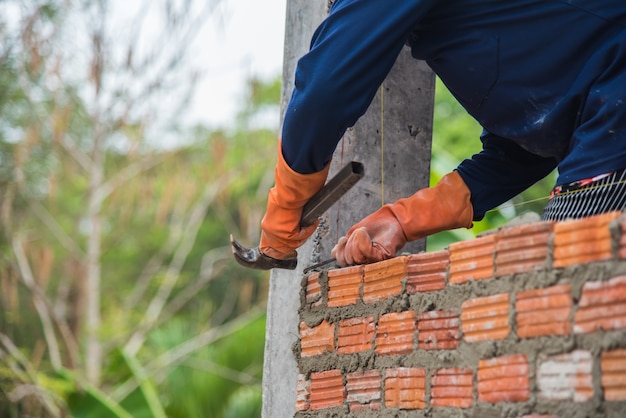 Professional installing red brick by hammer in construction site.