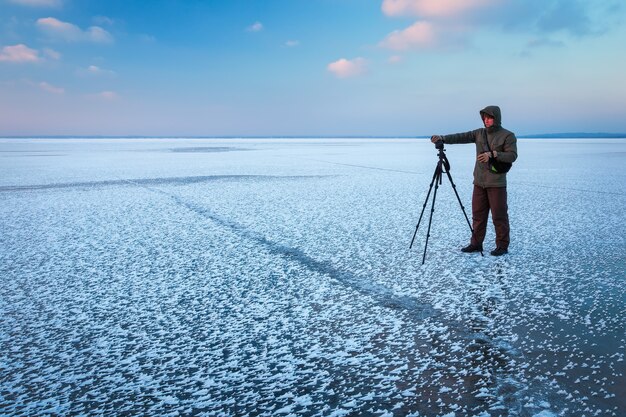 Профессионал на озере. Фотограф-натуралист делает снимки на берегу реки в зимний период с помощью зеркального фотоаппарата.