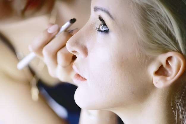 Foto trucco professionale nel salone di bellezza / master fa un trucco estivo professionale fresco di una bellissima modella nel salone