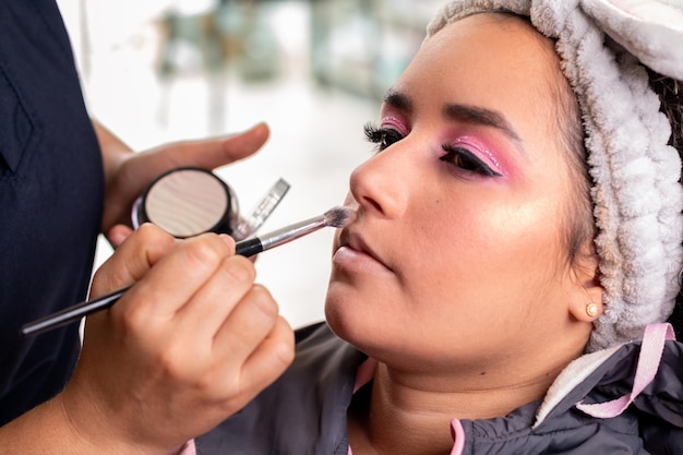 Профессиональный визажист наносит макияж на лицо латинской женщины кистью для макияжа