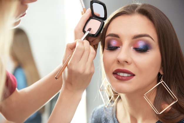 Professional makeup artist working with attractive young woman indoors