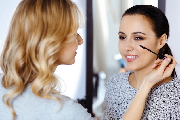 Professional makeup artist working with beautiful young woman. Bridal, fashion or nude style. Beauty concept.