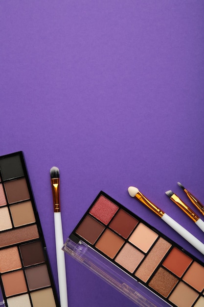 Professional makeup palette with brushes on purple background with copy space. Top view.