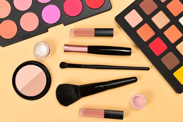 Professional makeup products with cosmetic beauty products, eye shadows, pigments, lipsticks, brushes and tools on beige background. Space for text or design.