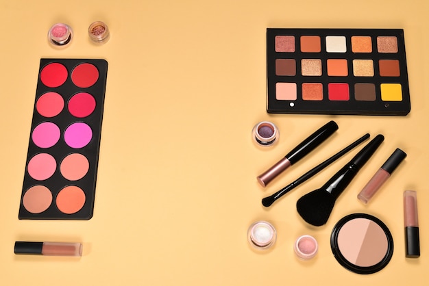 professional makeup products with cosmetic beauty products, eye shadows, pigments, lipsticks, brushes and tools on beige background. space for text or design.