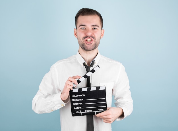 Foto attore maschio professionista pronto per le riprese di film, detiene il batacchio del film, isolato sulla parete blu.