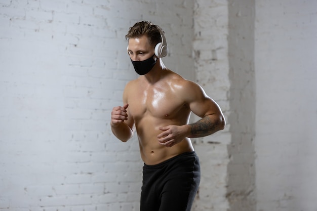 Professional male athlete training on brick wall background wearing face mask