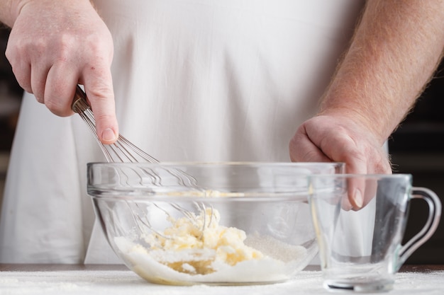 クリスマスのクッキーのために卵、バター、牛乳で生地を調理するプロの男性パン屋。