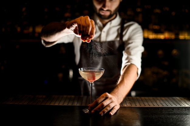 Professional male bartender serving a cocktail in the glass adding a lemon juice