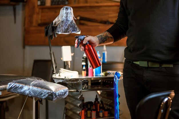 Il maestro professionista del tatuaggio caucasico barbuto maschio sta lavorando in un accogliente studio atmosferico