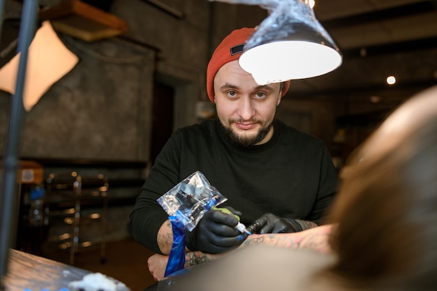 Professional male bearded caucasian tattoo master is working in cozy atmospheric studio