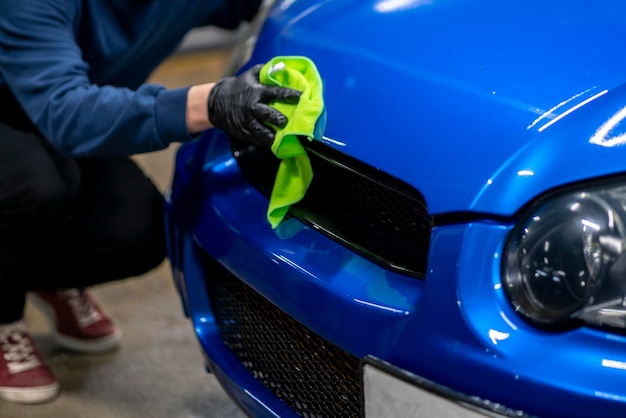 A professional male detailer doing some work on the blue car in\
workshop