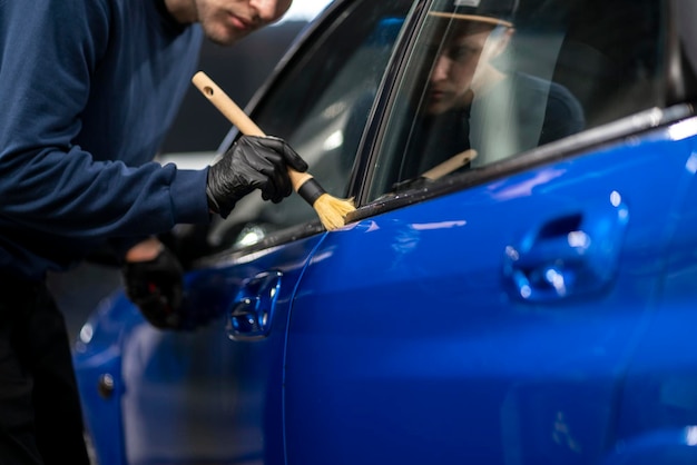 A professional male detailer doing some work on the blue car in workshop