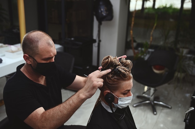 Professional male hairdresser dyeing hair of his client in salon. Haircutter cutting hair.