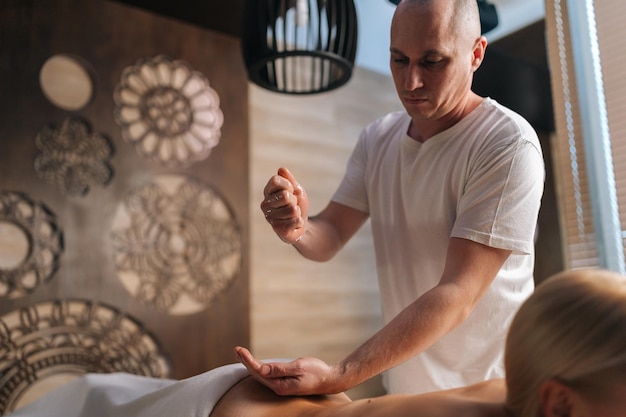 Foto massaggiatore professionista che versa olio da massaggio sulla mano che si prepara per il massaggio donna bionda nuda con