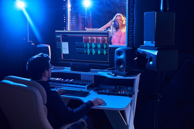 Фото Профессиональный звукорежиссер мужского пола, микширующий аудио в студии звукозаписи. технология производства музыки, девушка поет в микрофон