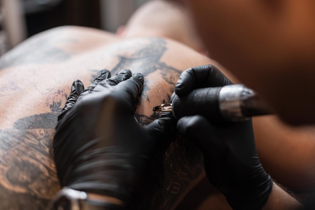 黒い手袋をはめたプロの男性のタトゥーマスターが、スタジオの男性の体にタトゥーを詰め込んでいます。タトゥーアーティストのワークフロー