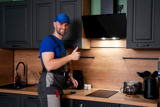 A professional male worker in uniform repairs a modern extractor hood in the kitchen