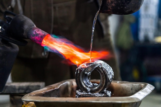 Фото Профессиональный рабочий-мужчина, использующий газовую горелку для плавления свинцового металла крупный план газовой горелки с огнем, направленным непосредственно на расплавленный металл.