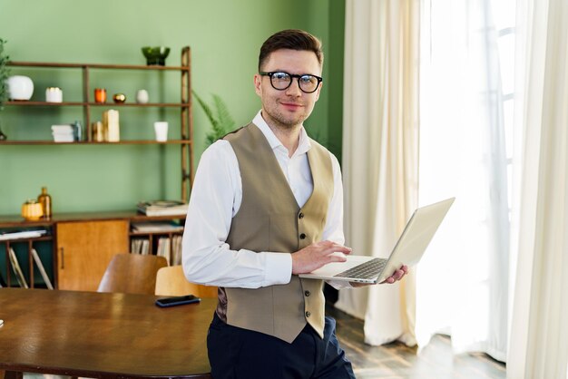 Foto un uomo professionista in giubbotto si trova con fiducia nel suo ufficio ben illuminato bilanciando un portatile che simboleggia