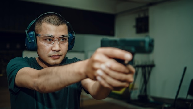 Foto l'uomo professionista che indossa cuffie e occhiali si sta esercitando a sparare con la pistola all'interno di un poligono di tiro