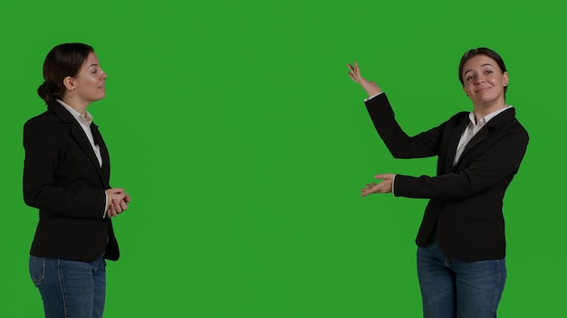 Professional manager pointing aside to show advertisement over greenscreen studio backdrop, creating example ad on blank copyspace. Young adult with suit showing ad icon in front of camera.