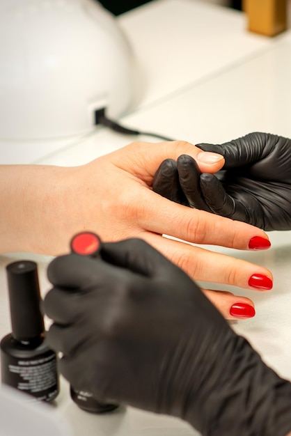 Professional manicure A manicurist is painting the female nails of a client with red nail polish in a beauty salon close up Beauty industry concept