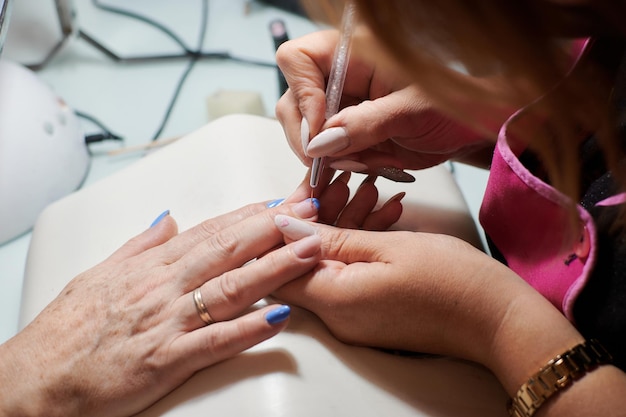 Профессиональный мастер маникюра ремонтирует и украшает ногти клиентки