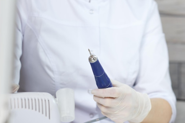 Professional manicurist in medical protective white gloves switch on nail drill in nail beauty salon