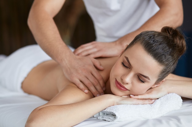 Professional massage therapist is treating a female patient in apartment