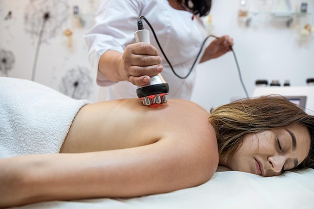 Photo professional masseuse performs a cellulite treatment on the whole body with a special device