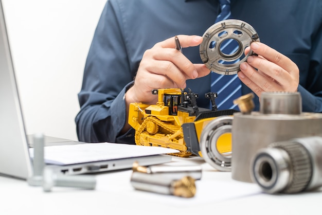 Professional mechanic engineer inspecting valve plate of\
hydraulic piston pump and writing reports for during working day in\
office, repair maintenance heavy machinery concept