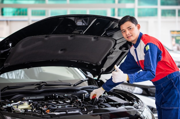 Il meccanico professionista in uniforme è controllare la qualità della nuova auto prima di consegnarla ai clienti. mentre si lavora nel centro di riparazione auto.