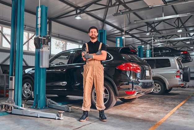 A professional mechanical employee of a car service workshop stand with crossed arms and tools looks