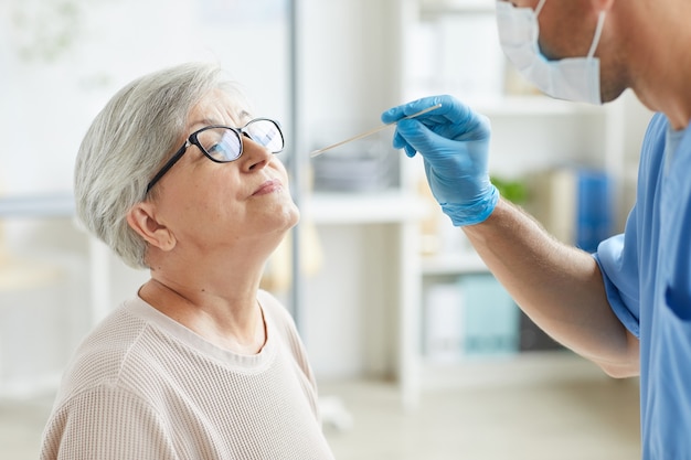 Professional medical worker wearing personal protective equipment testing senior woman for respiratory illnesses using test stick