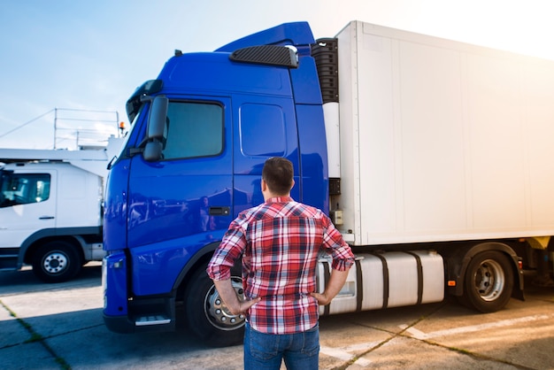 Профессиональный водитель грузовика средних лет в повседневной одежде смотрит на грузовик и собирается в долгую транспортную поездку.