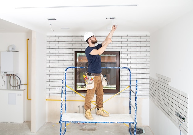 Professional in overalls with tools on the background of the repair site full length. Home renovation concept.