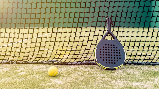 Профессиональная ракетка для паделя и желтый мяч за сеткой на зеленом газоне