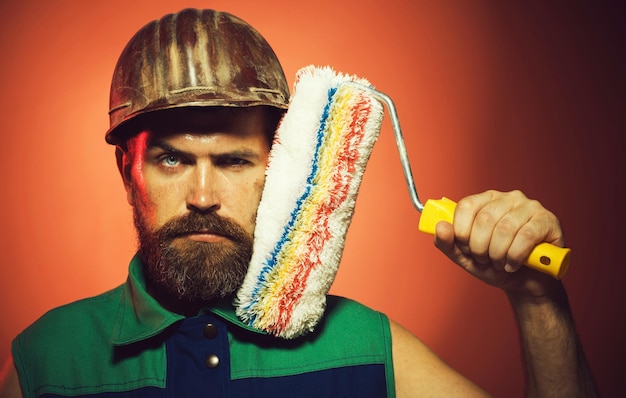 Professional painter man in helmet with paint roller bearded painter in uniform with painting tool