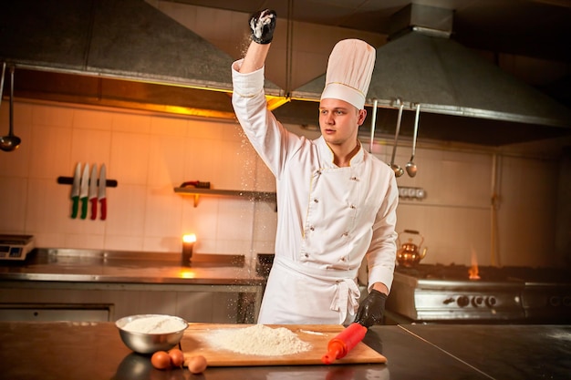 Professional pastry chef prepares dough with flour to make bread Italian pasta or pizza Flour is flying in the air on kitchen background Baking food concept