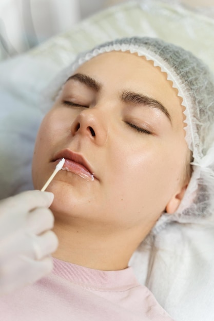 Professional permanent makeup artist applying anesthetic on client's lips before lip blushing procedure