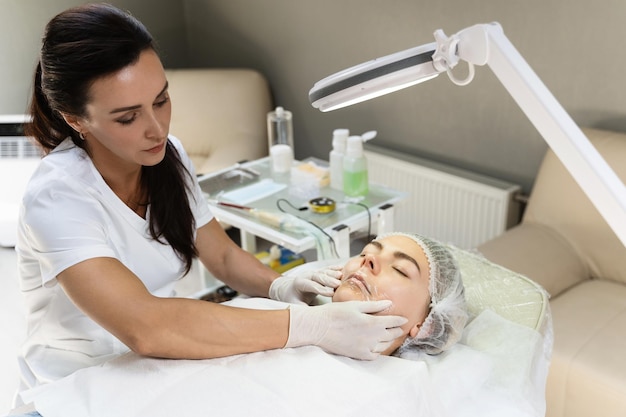 Профессиональный перманентный визажист наносит анестетик на губы клиента перед процедурой покраснения губ