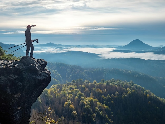 Professional photographer carry mirror camera and tripod on peak of rock dream foggy landscape